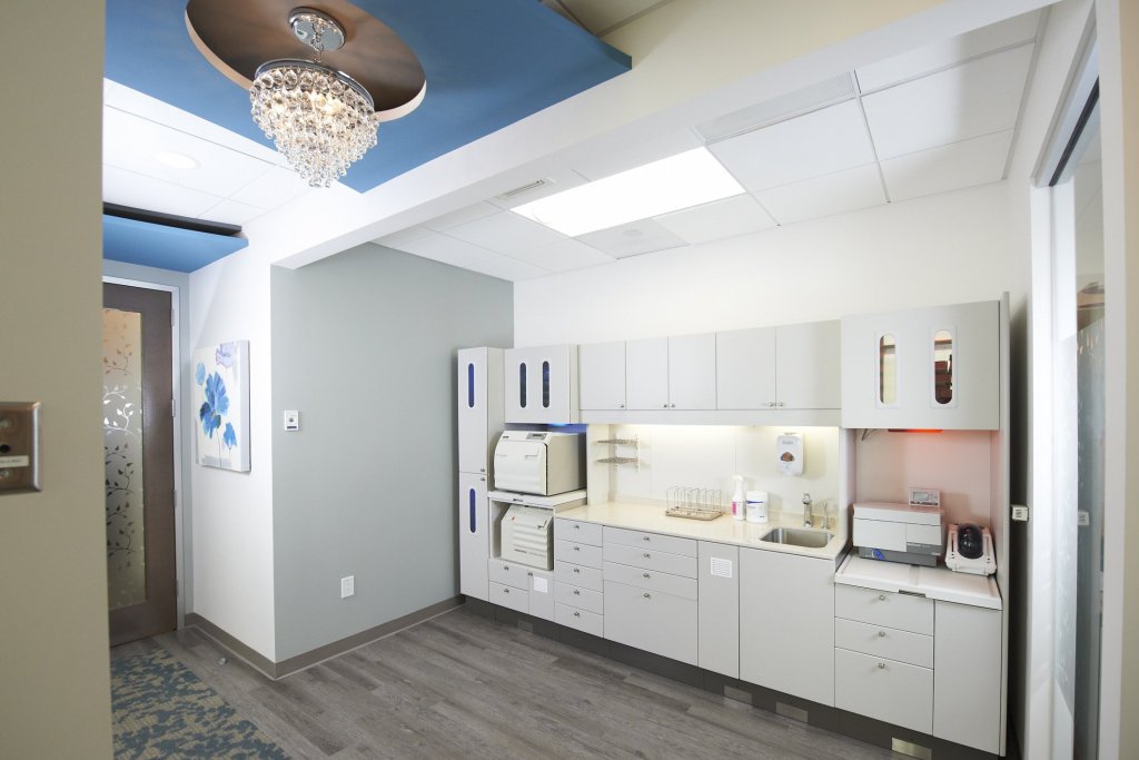Photo of a clean, modern dental office kitchen area with white cabinets, appliances, and a chandelier overhead.