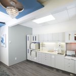 Photo of a clean, modern dental office kitchen area with white cabinets, appliances, and a chandelier overhead.