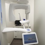 Photo of a dental X-ray machine in a clean, modern room with white walls and a digital display.