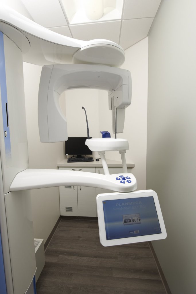 Photo of a dental X-ray machine in a clean, modern room with white walls and a digital display.